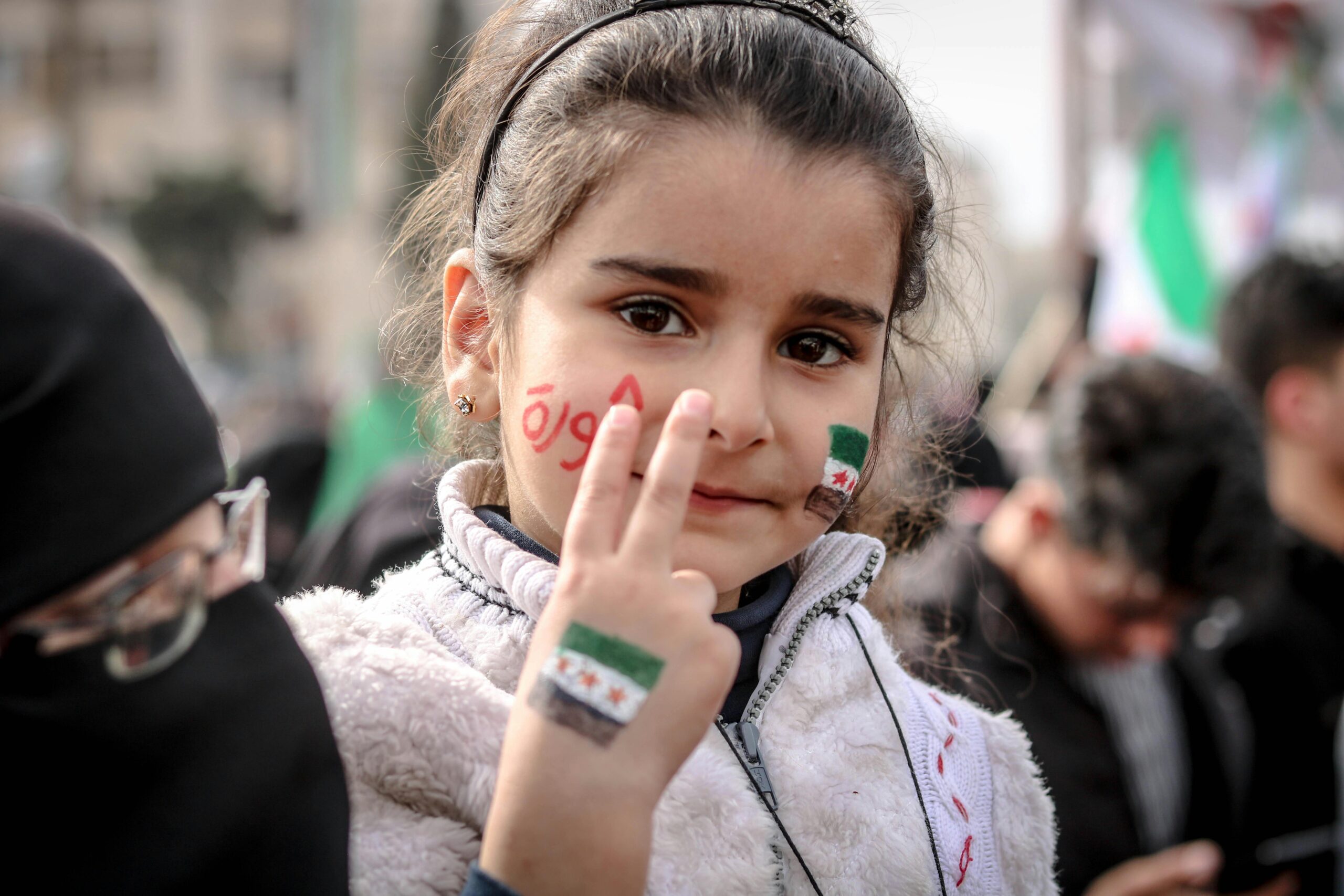A young Syrian girl shows a peace sign during a protest in Idlib, Syria, symbolizing hope and unity.
