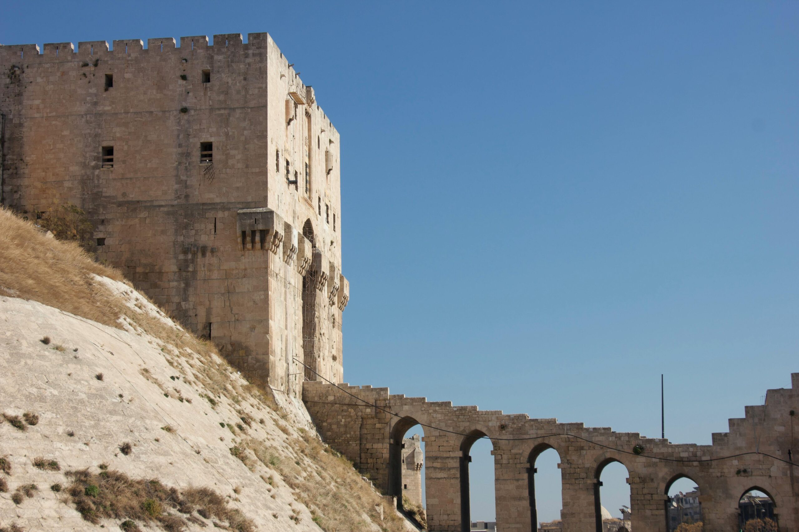 Ancient castle with arched structures under clear blue sky, featuring historical architecture.