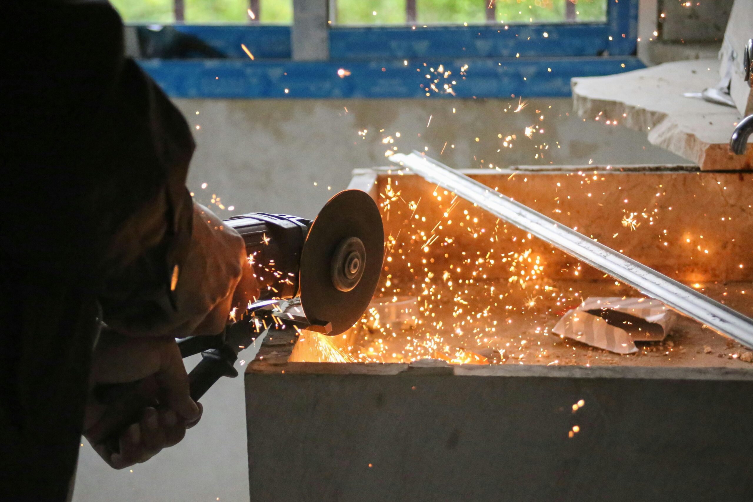 A worker in Latakia grinding metal, creating vibrant sparks in an industrial setting.